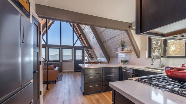Une cuisine moderne dotée d’un grand îlot central, de meubles de rangement aux couleurs sombres et offrant une vue sur l’extérieur.