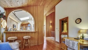 A cozy living room with a wooden ceiling, a dining area with a table and chairs, and a kitchen with wooden cabinets and a large mirror. - HOA  w/ Pools & Hot Tubs, Dogs Ok- Northstar On The Course (Truckee)