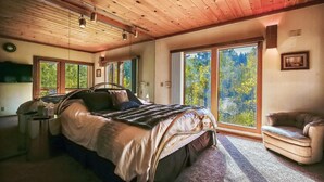 A bedroom with a large bed, a chair, and a view of a forest through a sliding door. - HOA  w/ Pools & Hot Tubs, Dogs Ok- Northstar On The Course (Truckee)