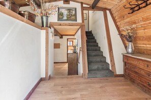 A wooden staircase leading to a second floor, with a rustic interior design including a wooden wall, a metal bucket, and a vase with dried flowers.