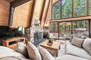 A spacious living area with a stone fireplace, large windows, and a flat-screen TV. - Short Drive to the Beach, Hot Tub, Large Deck - All Decked Out (Carnelian Bay)