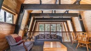 A cozy loft-style room with a sloped ceiling, wooden beams, a sofa, a coffee table, and a dining table with chairs. - Short Drive to the Beach, Hot Tub, Large Deck - All Decked Out (Carnelian Bay)