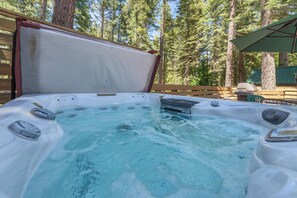 Ein Whirlpool mit einer Holzterrasse und Blick auf hohe Bäume.