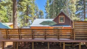 A wooden deck with benches, a covered area with an umbrella, and a cabin with a metal roof surrounded by trees. - Walk to Tahoe Park Private Beach, Hot Tub, Dogs OK- Cedar Crest (Tahoe City)