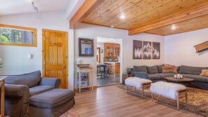 A living room with a sofa, ottoman, and coffee table, wooden flooring, and a ceiling with exposed beams. - Walk to Tahoe Park Private Beach, Hot Tub, Dogs OK- Cedar Crest (Tahoe City)
