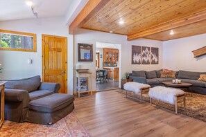 A living room with a sofa, ottoman, and coffee table, wooden flooring, and a ceiling with exposed beams. - Walk to Tahoe Park Private Beach, Hot Tub, Dogs OK- Cedar Crest (Tahoe City)
