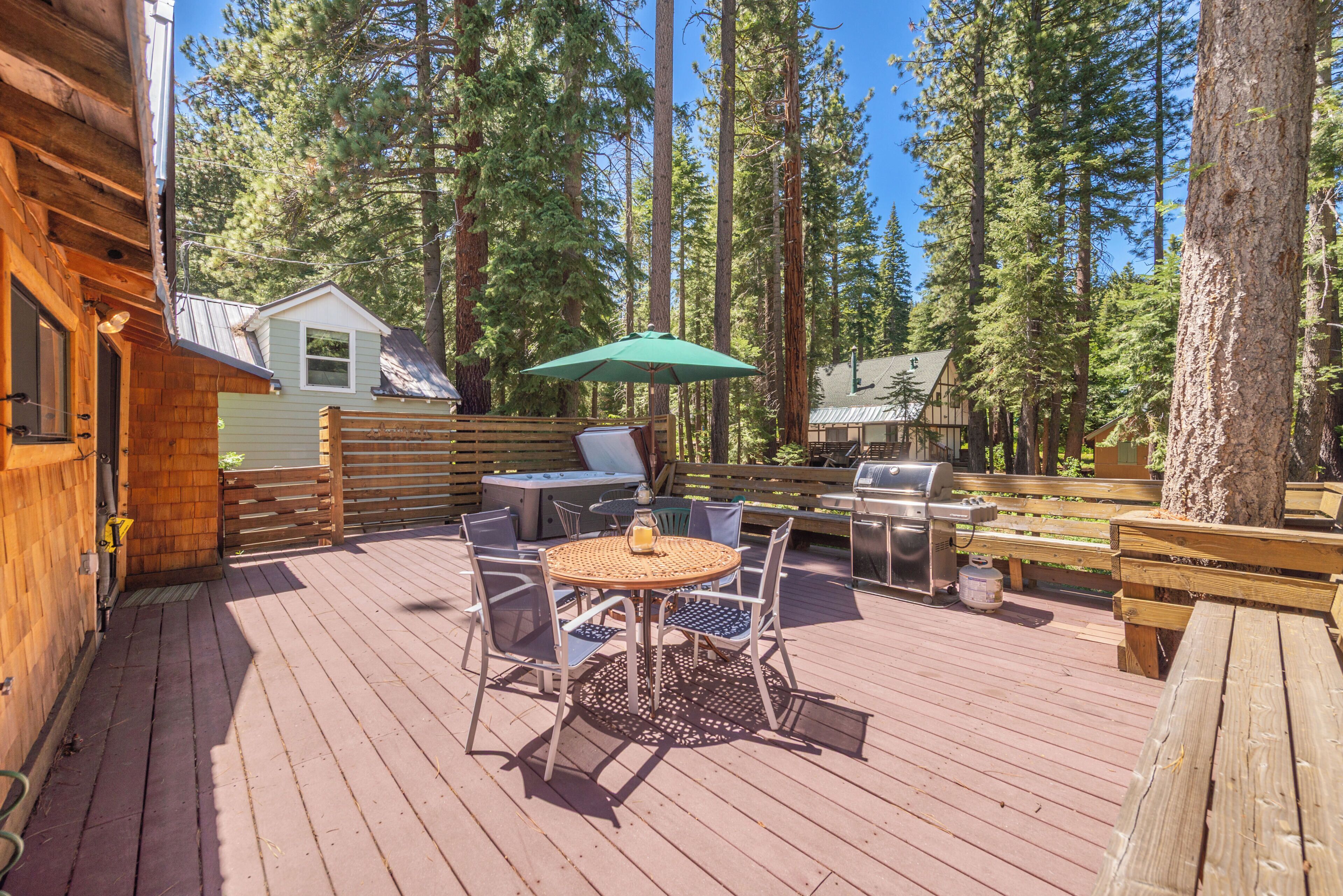 A wooden deck with a table and chairs, a grill, and a green umbrella.