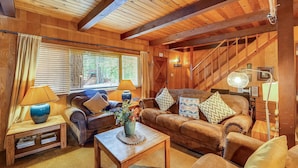 A cozy wooden-furnished living room with a sofa, armchairs, a coffee table, and a staircase.