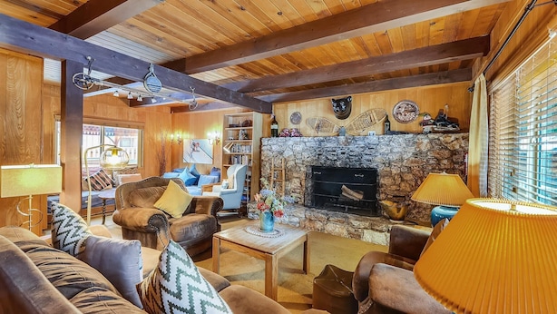 A cozy living room with a stone fireplace, wooden beams, and comfortable seating.