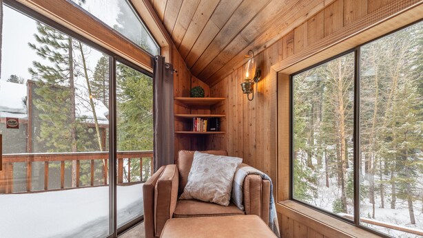 A cozy cabin interior with a cushioned bench, wooden shelves, and large windows offering a view of a snowy forest. - Alpine Getaway - N. Lake Tahoe, Hot Tub, Mountain Views (Alpine Meadows)