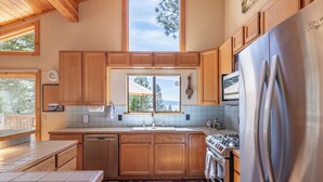 A kitchen with wooden cabinets, a stainless steel refrigerator, and a window with a view of trees and mountains. - Overlook Cabin, Good View, Walk to Tahoe City, Wood Stove (Tahoe City)
