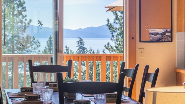 A dining area with a view of a lake and mountains, wooden chairs, and a table set with plates and glasses. - Overlook Cabin, Good View, Walk to Tahoe City, Wood Stove (Tahoe City)