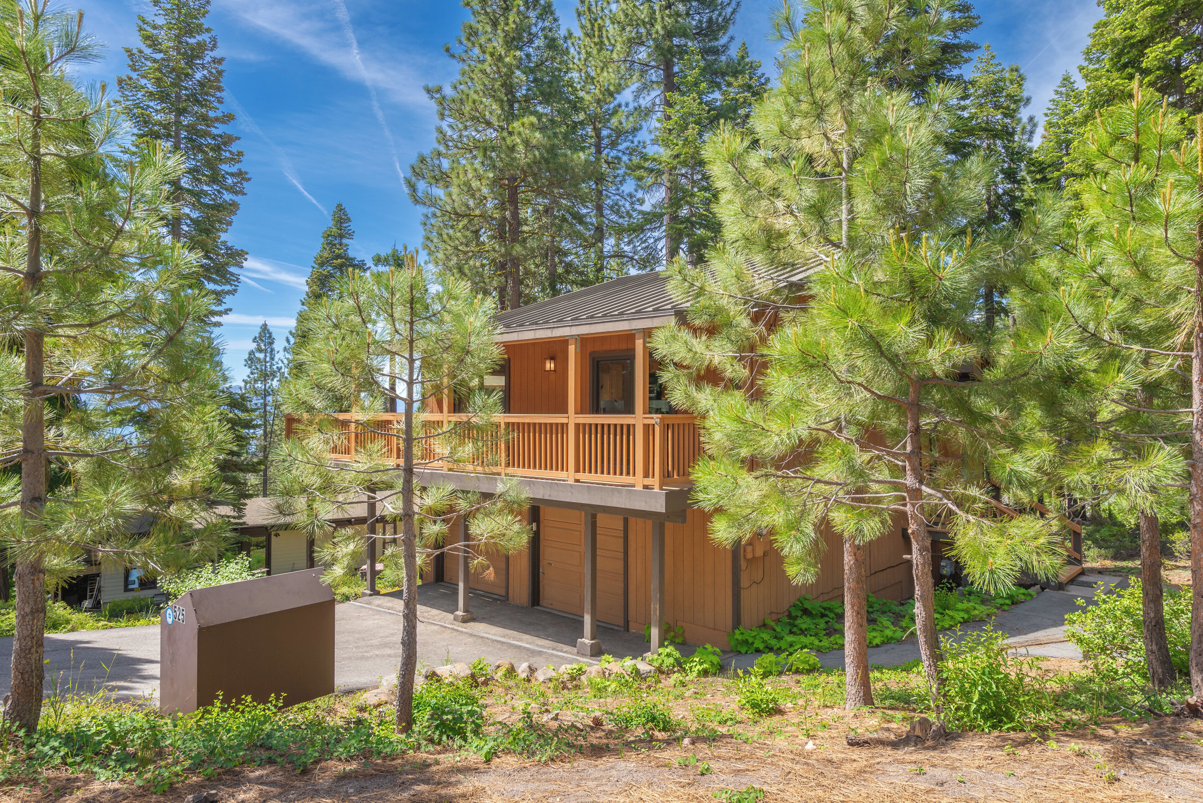 A two-story wooden cabin surrounded by pine trees.
