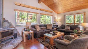 A cozy living room with a fireplace, comfortable seating, and large windows offering a view of the outdoors. - Overlook Cabin, Good View, Walk to Tahoe City, Wood Stove (Tahoe City)