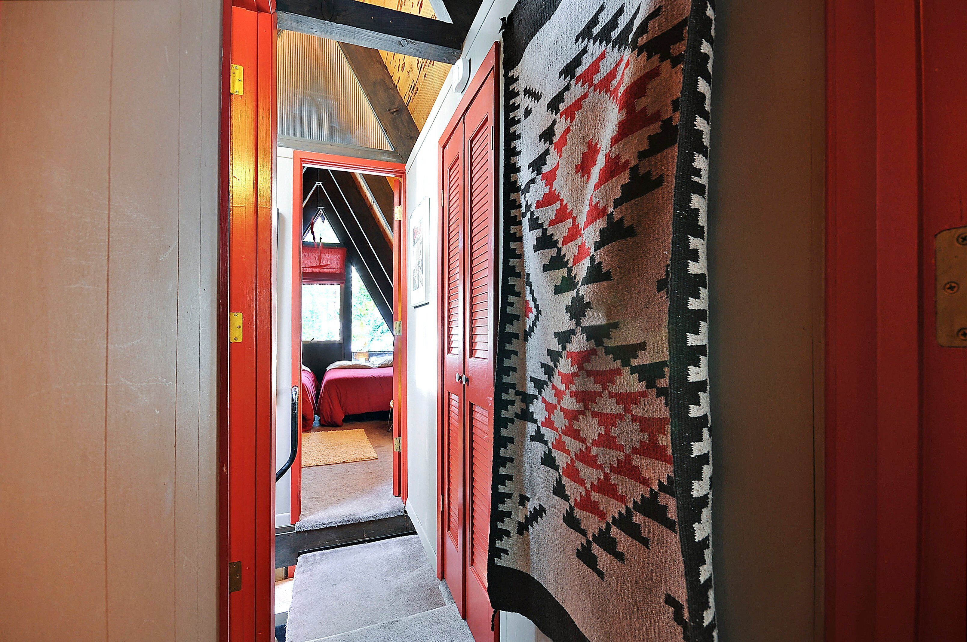 Un couloir avec une porte rouge, un tapis à motifs et un lit à l’arrière-plan.
