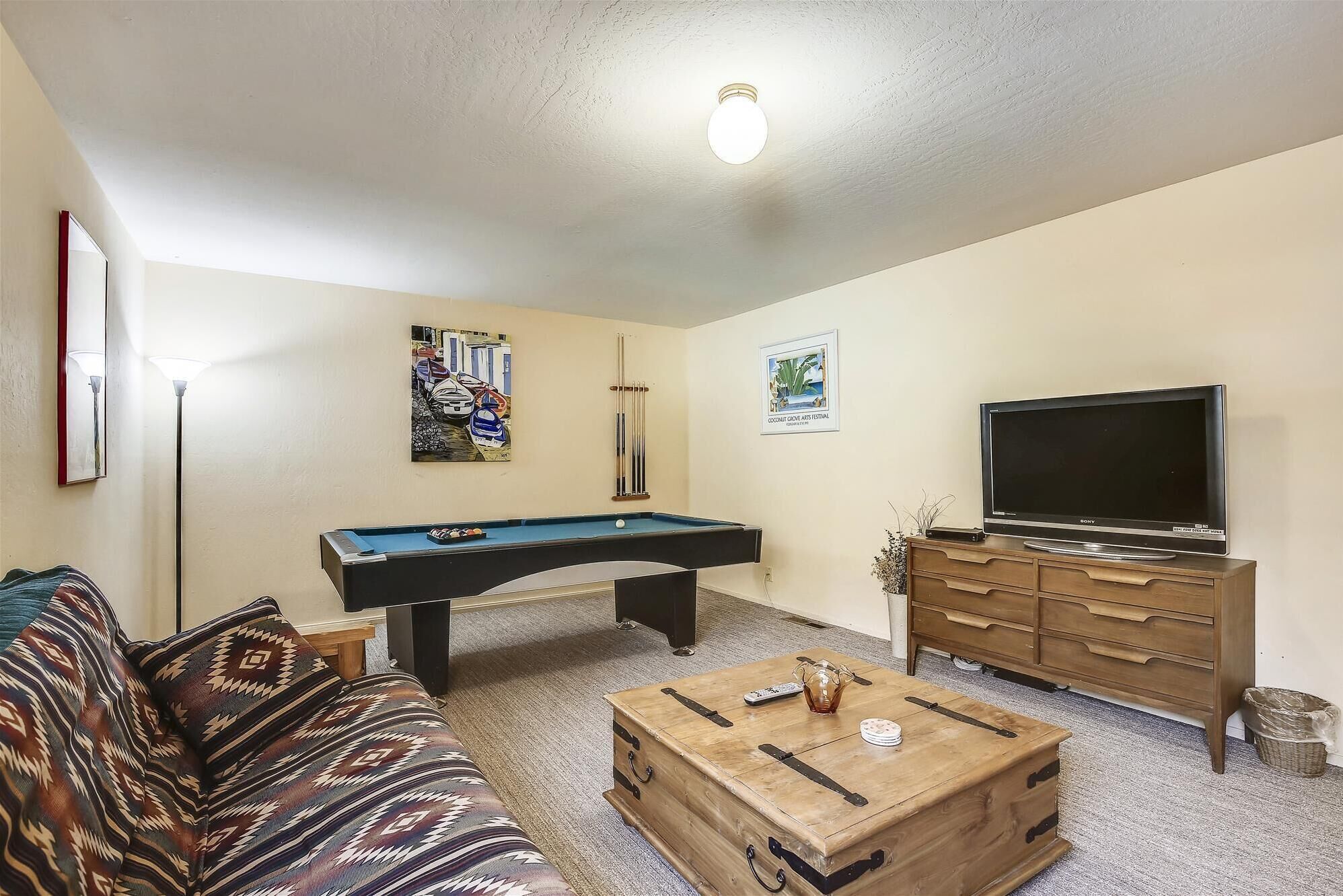 A living room with a pool table, sofa, coffee table, TV, and artwork on the walls.