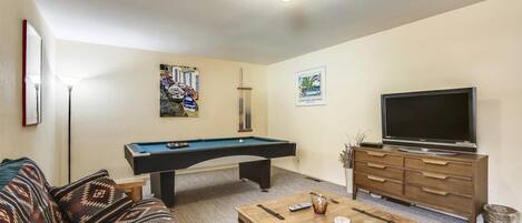 A living room with a pool table, sofa, coffee table, TV, and artwork on the walls.