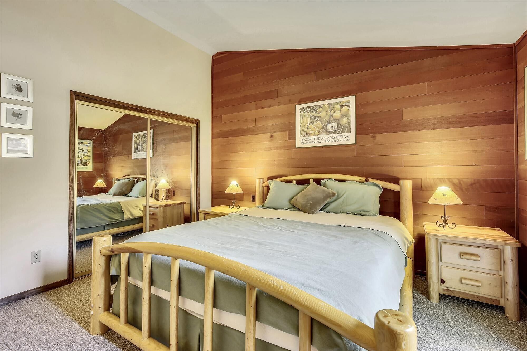 Ein Schlafzimmer mit einem Holz-Kopfteil, einem großen Spiegel, zwei Nachttischen mit Lampen und einem gerahmten Bild an der Wand.