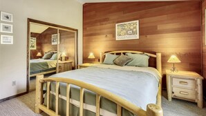 Un dormitorio con cabecera de madera, un espejo grande, dos mesitas de noche con lámparas y un cuadro en la pared.