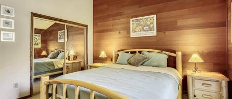 Ein Schlafzimmer mit einem Holz-Kopfteil, einem großen Spiegel, zwei Nachttischen mit Lampen und einem gerahmten Bild an der Wand.