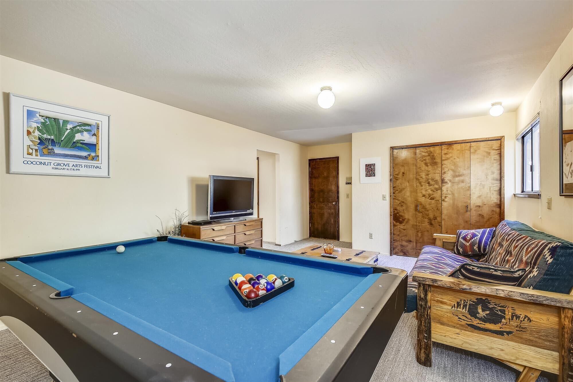 A room with a pool table, a television, a wooden cabinet, and a couch.