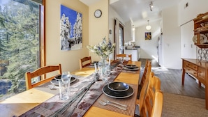 Un comedor con una larga mesa de madera dispuesta para cuatro personas, un jarrón de flores y un cuadro en la pared.