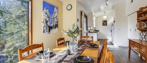 A dining area with a long wooden table set for four, a vase of flowers, and a painting on the wall.