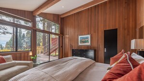 Een ruime slaapkamer met een groot bed, houten wanden, een zwart hoofdeinde en uitzicht op een trap die naar buiten leidt.