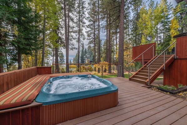 Un jacuzzi en una terraza de madera rodeado de árboles altos.