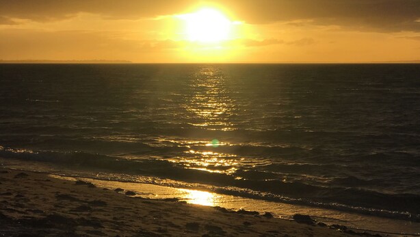 A sunset over the ocean with the sun reflecting on the water.