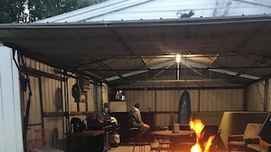 A covered outdoor area with a barbecue grill, chairs, and a television.