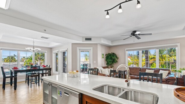 A spacious kitchen with a large island, a dining area, and a living room with a view of palm trees. - Siesta Breeze Retreat | Luxury Condo on SK w/ Heated Pool, Walking Distance to Beach & Village! (Siesta Key)