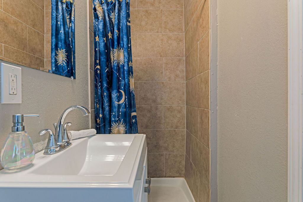 Un baño con lavamanos blanco, espejo y cortina de ducha con diseño celeste.
