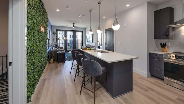Una cocina moderna con una isla central, taburetes de bar, una estufa integrada y un jardín vertical verde.