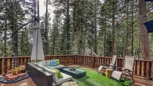A wooden deck with outdoor furniture, including a sofa and chairs, surrounded by a forest.