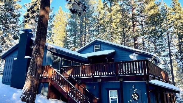 A cabin with a wooden staircase leading to a deck, surrounded by snow-covered trees.