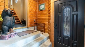 A wooden interior with a black door, a welcome bear statue, and a framed picture on the wall.