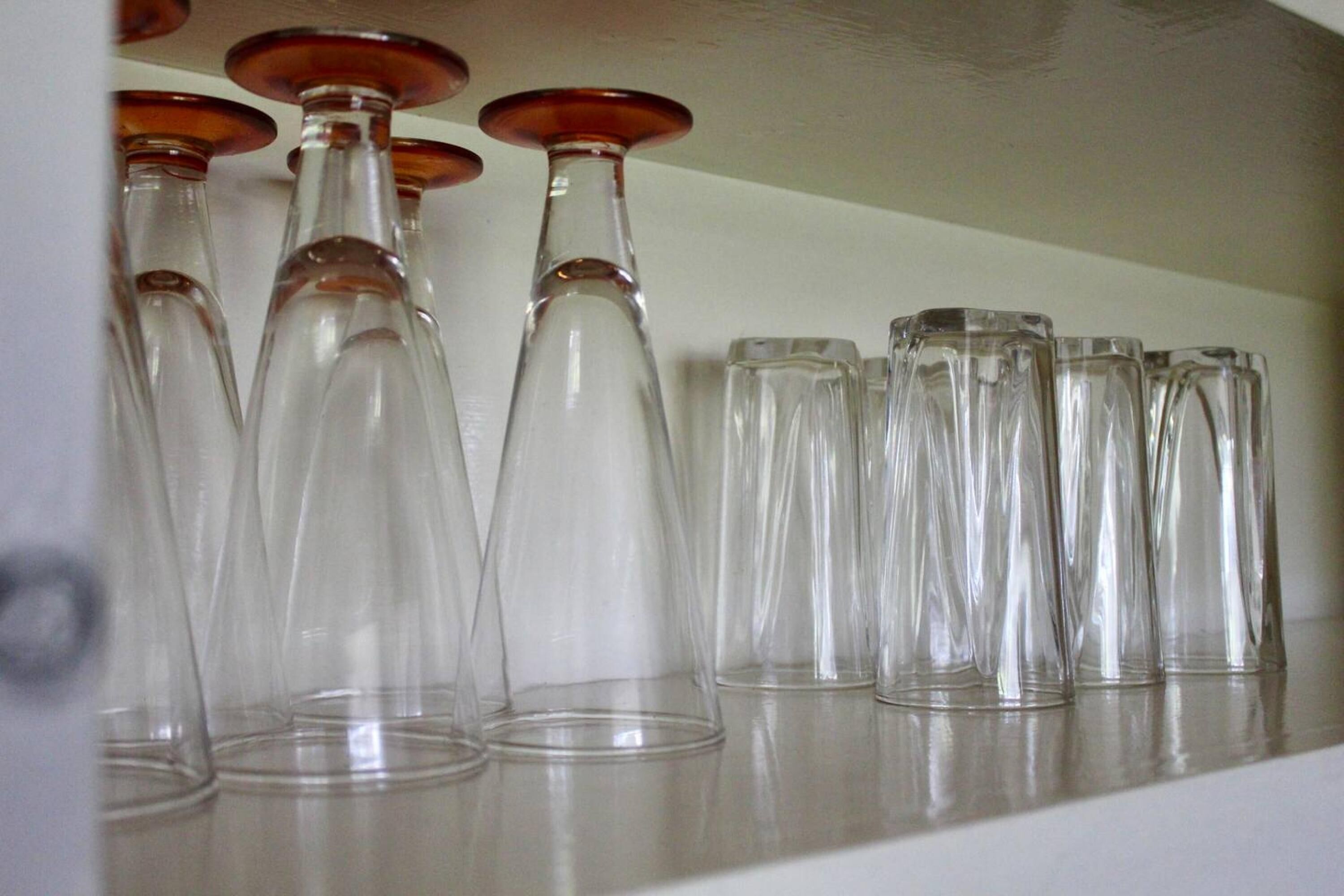 Une collection de verres à vin transparents, dont les bords sont rouges, disposés sur une étagère.