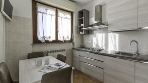 Une cuisine moderne équipée d’une cuisinière à gaz, d’un évier en acier inoxydable et de meubles de rangement en bois clair. On y trouve une table à manger avec des chaises, ainsi qu’une fenêtre avec des rideaux.