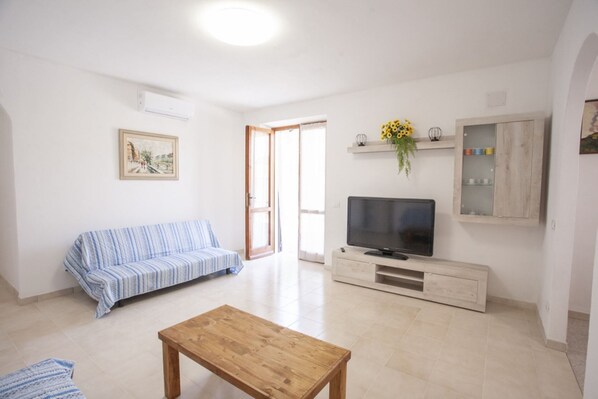 A living room with a sofa, a coffee table, a TV on a wooden cabinet, and a painting on the wall.