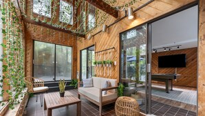 Un espace patio accueillant, doté d’un plancher en bois, d’un canapé, d’une table et de chaises. On y trouve également des plantes en pot et un téléviseur fixé au mur.