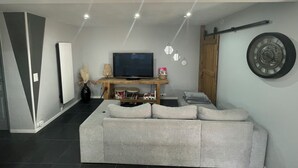 Una sala de estar moderna con un sofá gris, un televisor de pantalla plana sobre un mueble de madera y un reloj decorativo en la pared.