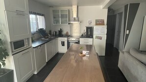 Una cocina moderna con una isla central, armarios blancos y un comedor con una mesa de madera y bancos.
