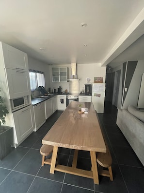 A modern kitchen with a central island, white cabinetry, and a dining area with a wooden table and benches. - L Imprévu est une Maison Individuelle (Sennecey-le-Grand)