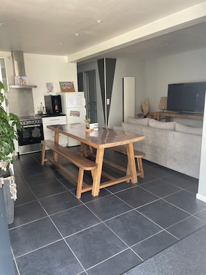 A modern kitchen with a wooden table and bench, a built-in oven, and a refrigerator. - L Imprévu est une Maison Individuelle (Sennecey-le-Grand)