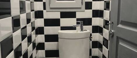 Et lille, kompakt badeværelse med toilet, håndvask og et vindue over håndvasken.