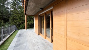 Un edificio moderno in legno con patio in pietra, ampie porte scorrevoli in vetro e ringhiera in metallo.