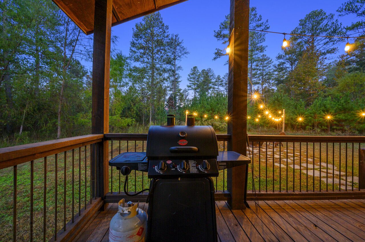 Een barbecue op een houten terras, met uitzicht op een bebost gebied.