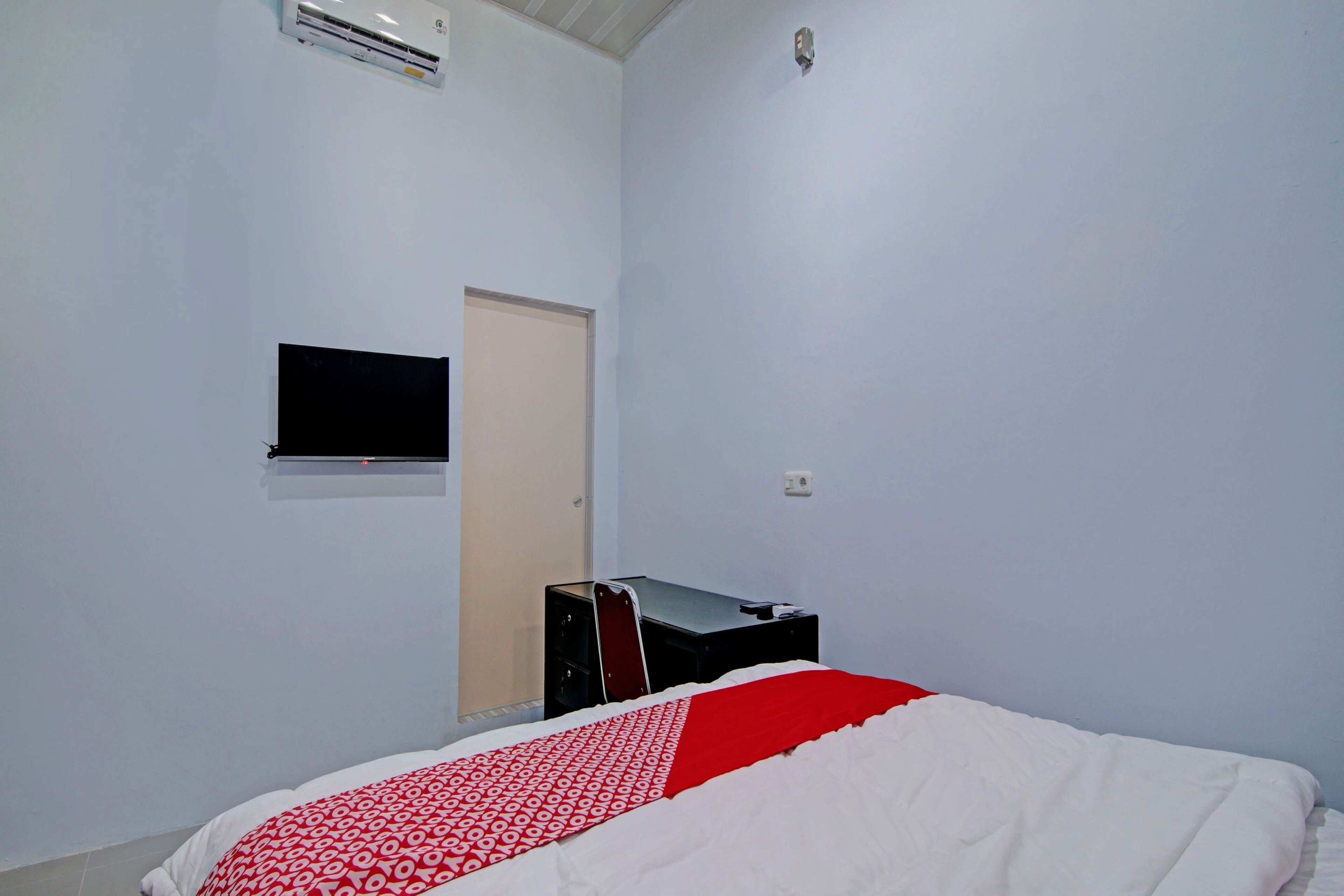 Quarto com cama, televisão na parede e escrivaninha com cadeira.
