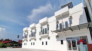 A multi-story white building with balconies, air conditioning units, and a storefront with glass doors. - Hotel O Penginapan Sarinah SyariahNearRM Beringin Indah (Pangkalan Kuras)